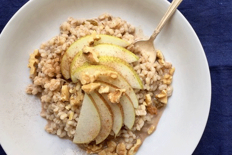 A white bowl of barley topped with pears and walnuts on a blue tablecoth