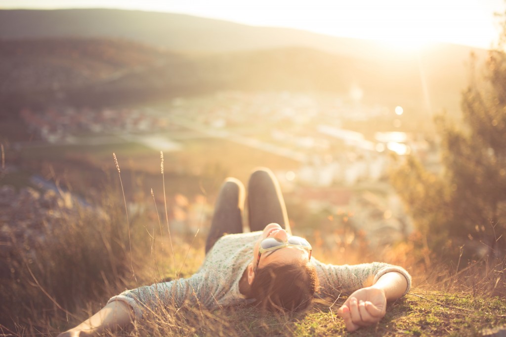 arefree happy woman lying on green grass meadow on top of mounta