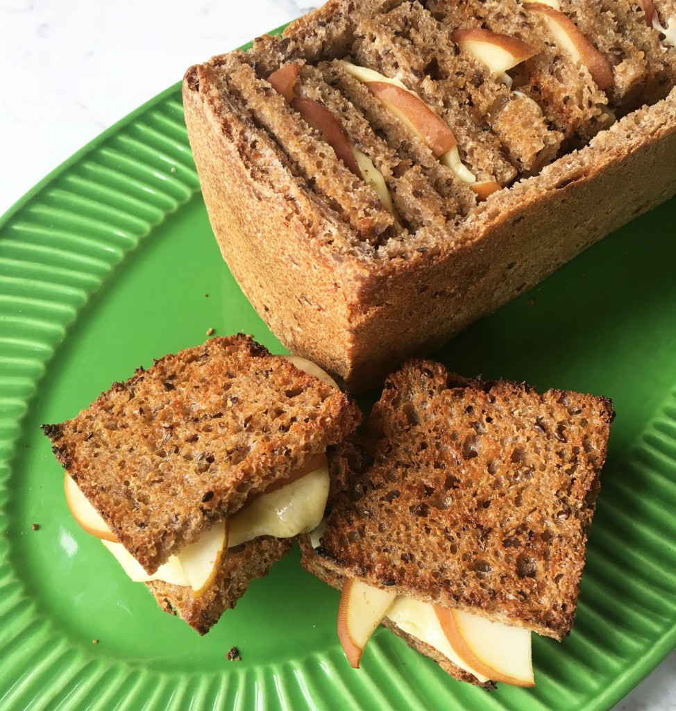 Little grilled cheese and pickled pear snadwiches stuffed inside a hollowed out bread loaf on a green plate